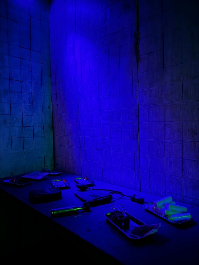 A dimly lit laboratory with a dark countertop holding various tools and equipment under a blue light.